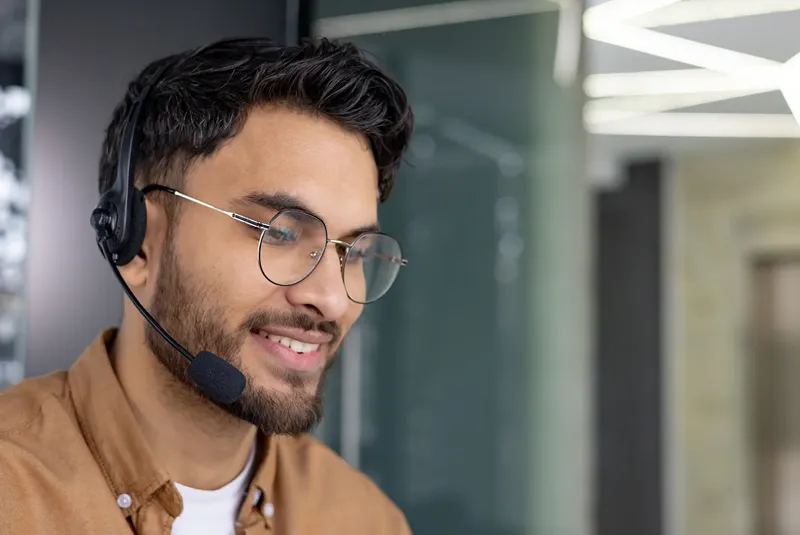 Jetzt als Neukunde registrieren und von hochwertigen Systemen der TAROX Eigenmarke über Produkte führender Hersteller bis hin zu ergänzenden Cloud‑ und Security‑Lösungen profitieren. Jetzt als Neukunde registrieren und von hochwertigen Systemen der TAROX Eigenmarke über Produkte führender Hersteller bis hin zu ergänzenden Cloud‑ und Security‑Lösungen profitieren. Foto eines jungen Mannes mir Brille und Vollbart, der ein Headset trägt.