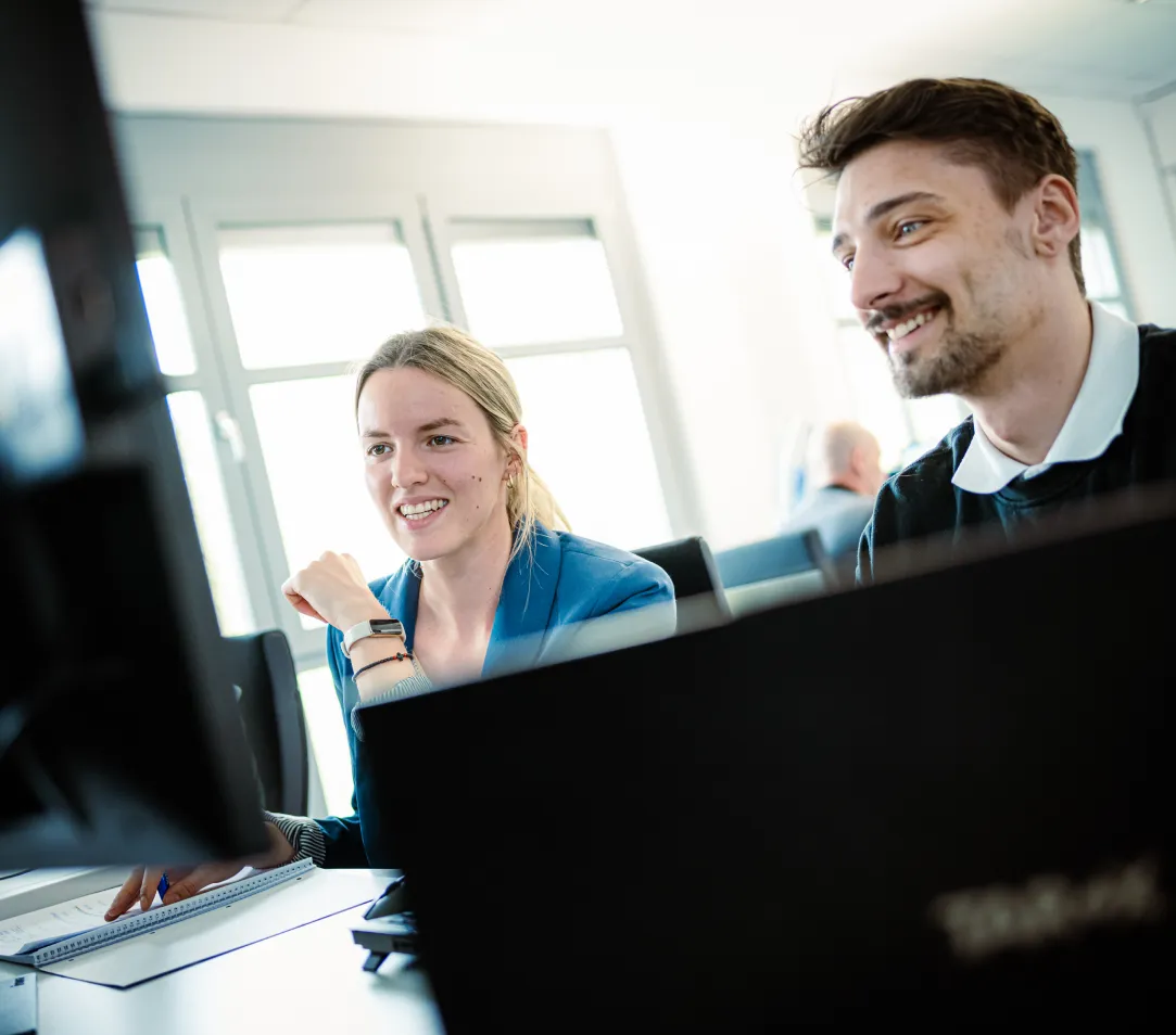 Wir setzen auf langfristige Kunden- und Partnerschaften und begleiten Sie von Anfang an zuverlässig und umfassend – mit klarem Fokus auf Ihren nachhaltigen Erfolg. 2 lächelnde Mitarbeiter sitzen gemeinsam an einem Schreibtisch.
