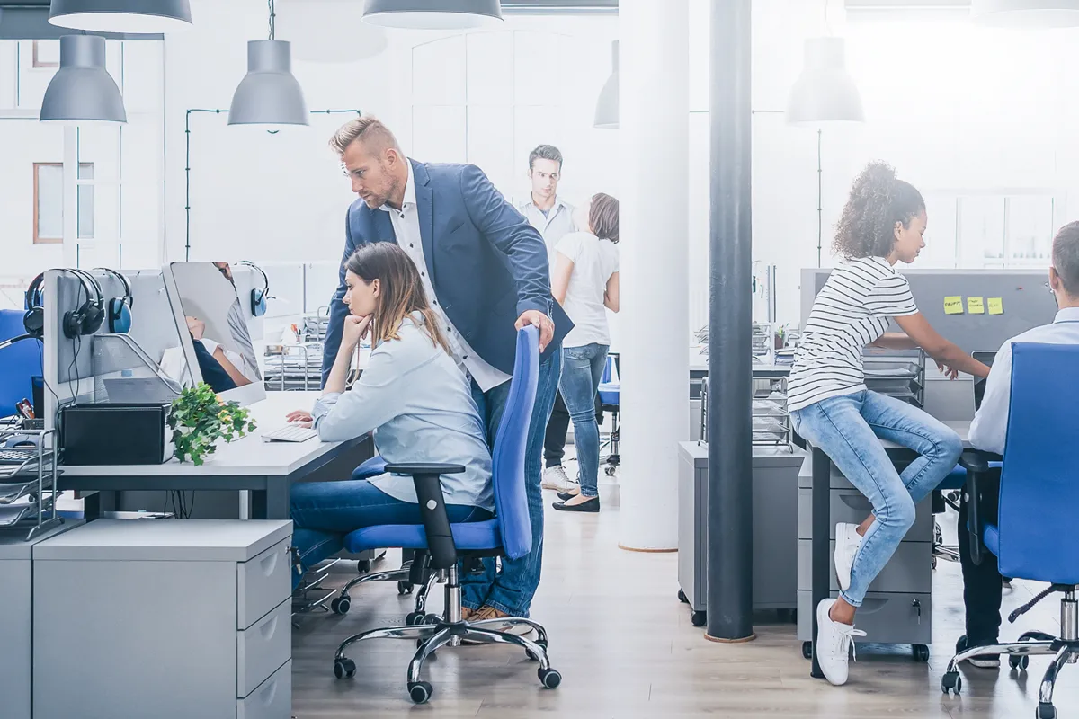 Lerne bei der Ausbildung im Groß- und Außenhandel alle Prozesse rund um Einkauf, Vertrieb, Transport und Lieferung unserer Produkte kennen. Foto einer jungen Auszubildenden, die an ihrem Arbeitsplatz in einem Großraumbüro sitzt und angeleitet wird.
